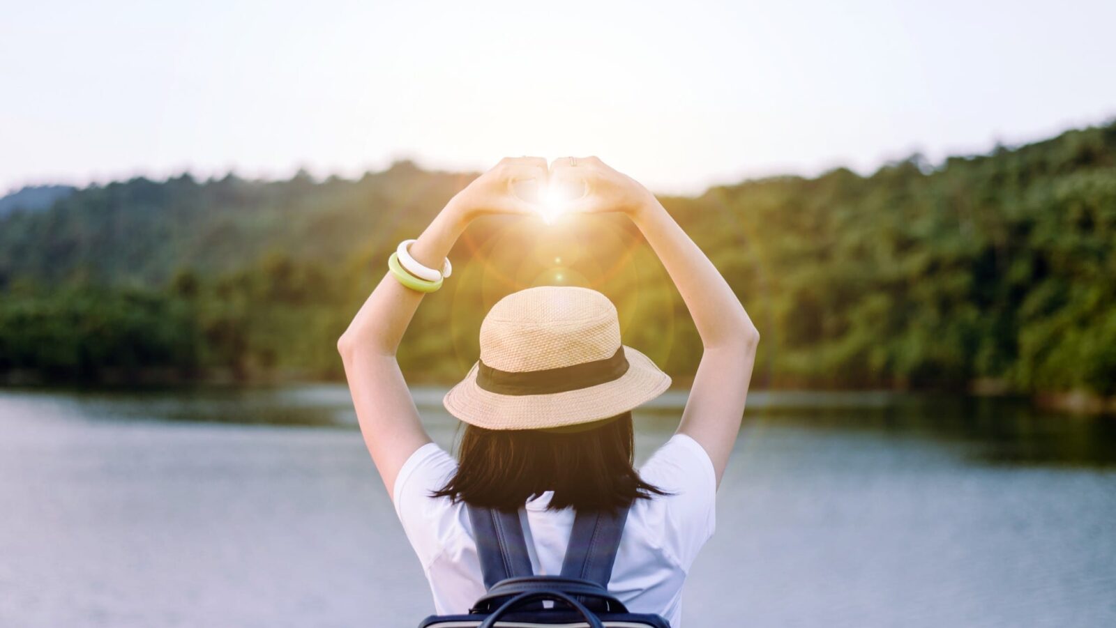 woman holding hands in a heart over the sun at sunset