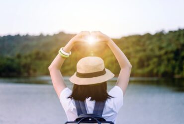 woman holding hands in a heart over the sun at sunset