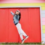 girl in sneakers jumping in front of colorful house