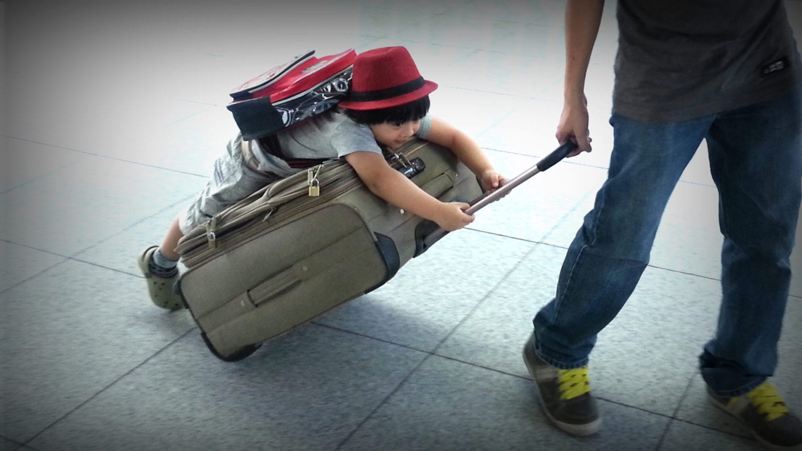child wearing backpack riding on suitcase