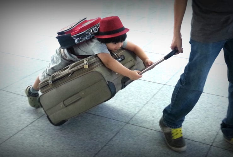 child wearing backpack riding on suitcase