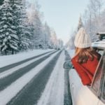 Teen girl in car over snowy forest on winter road trip.