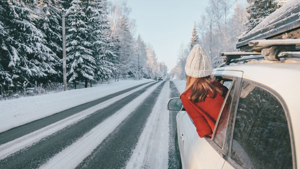 Teen girl in car over snowy forest on winter road trip.