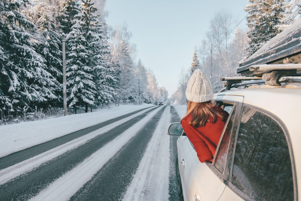 Teen girl in car over snowy forest on winter road trip.