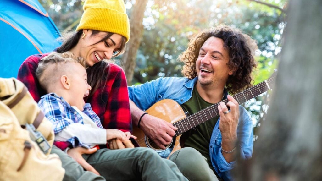 young family camping and parent playing guitar to a delighted child