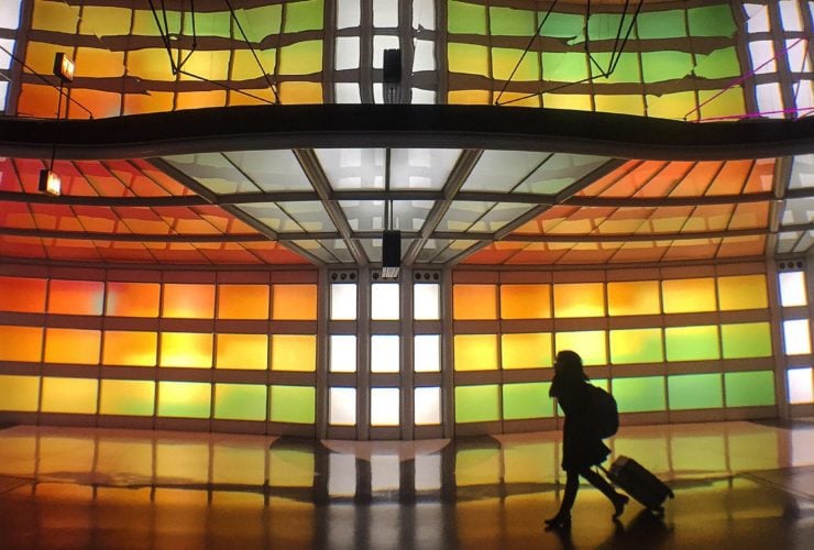 Person rolling luggage in front of stained glass display in airport terminal