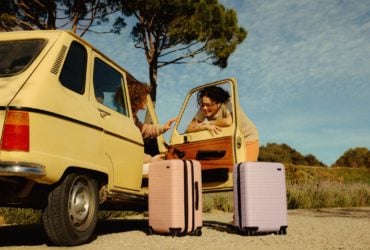People hanging out near a yellow car with light purple and pink Away luggage