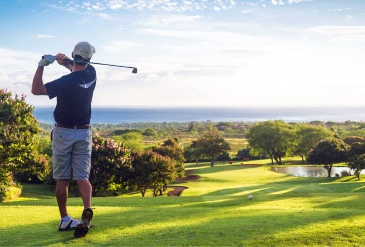 Man hitting golf ball down hill towards ocean and horizon (Photo: Shutterstock)