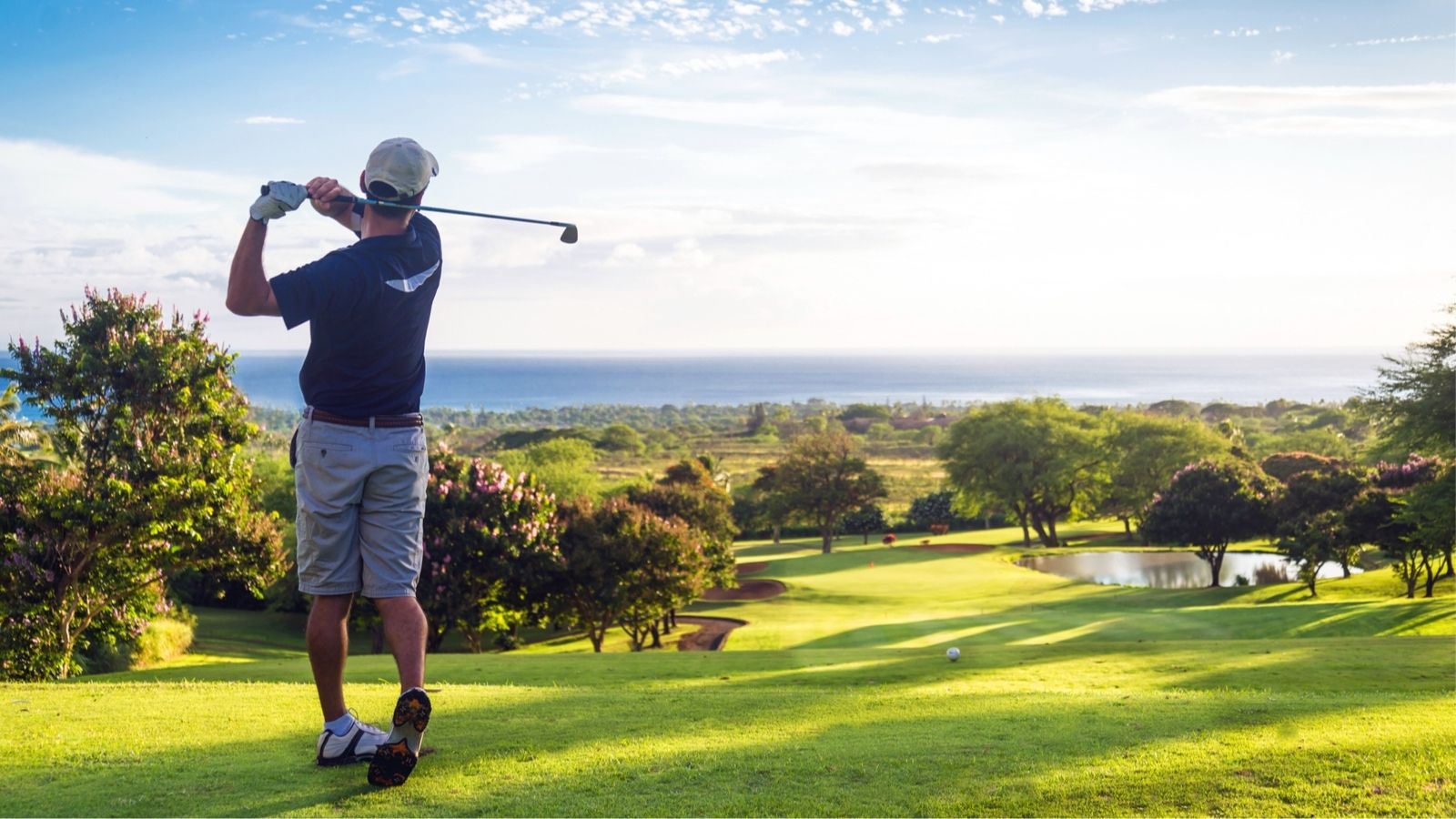 Man hitting golf ball down hill towards ocean and horizon (Photo: Shutterstock)