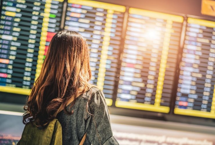Woman in airport terminal looking at arrivals and departures board (Photo: Shutterstock)
