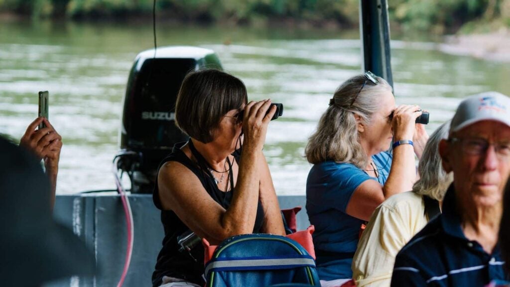 senior travelers on a Road Scholar tour to Costa Rica, using binoculars to look at wildlife from a boat