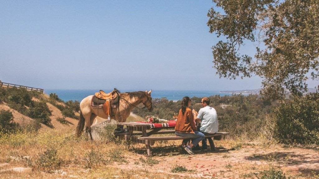 Horseback riding is a popular thing to do in Santa Barbara. Los Padres Outfitters horse and people picnicking with a view of the ocean on a sunny day.