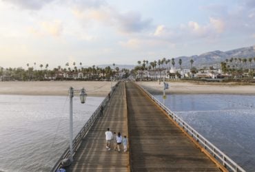 A family walking down Stearns Wharf with downtown Santa Barbara and beaches in the background. Stearns Wharf and downtown are popular things to do in Santa Barbara.