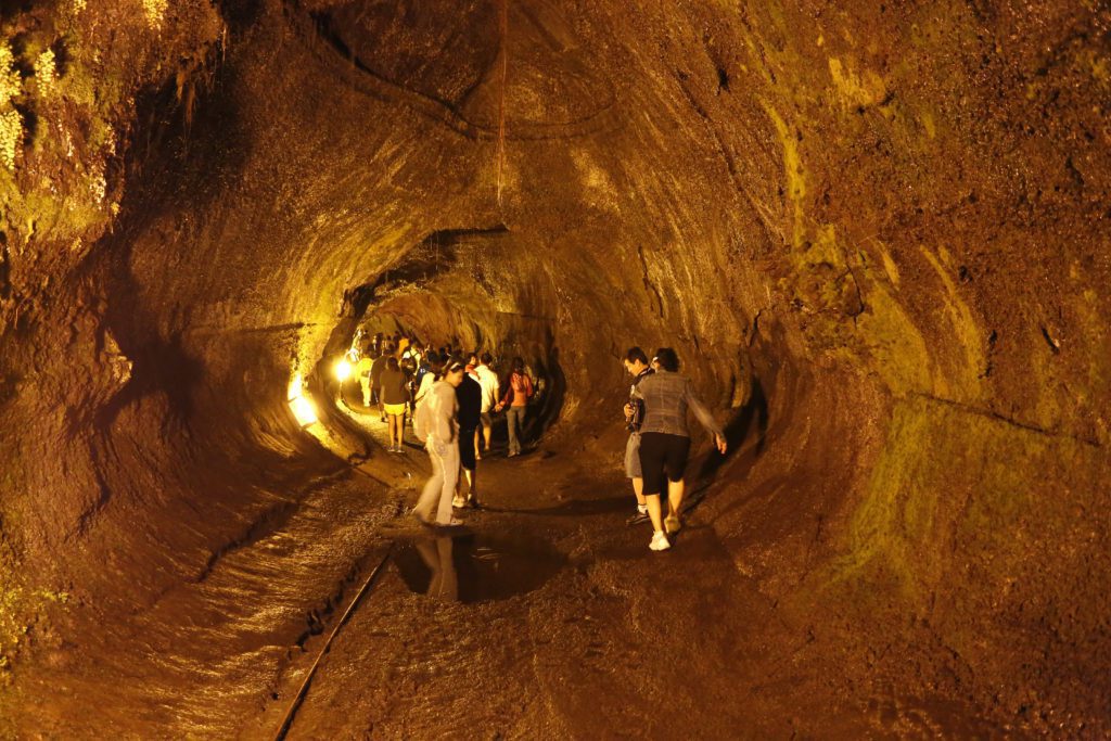 orang-orang berjalan di sepanjang bagian Thurston Lava Tube yang diterangi cahaya di Taman Nasional Gunung Api Hawaii
