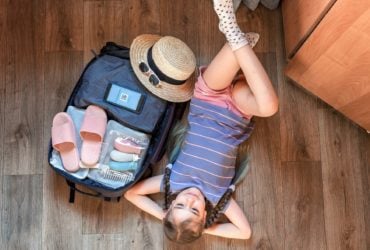 girl relaxing next to packed suitcase