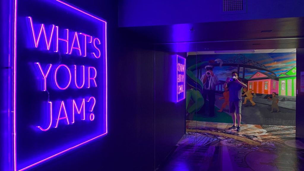 interior of the JAMNOLA installation in New Orleans, featuring a neon sign that reads "What's Your Jam?"