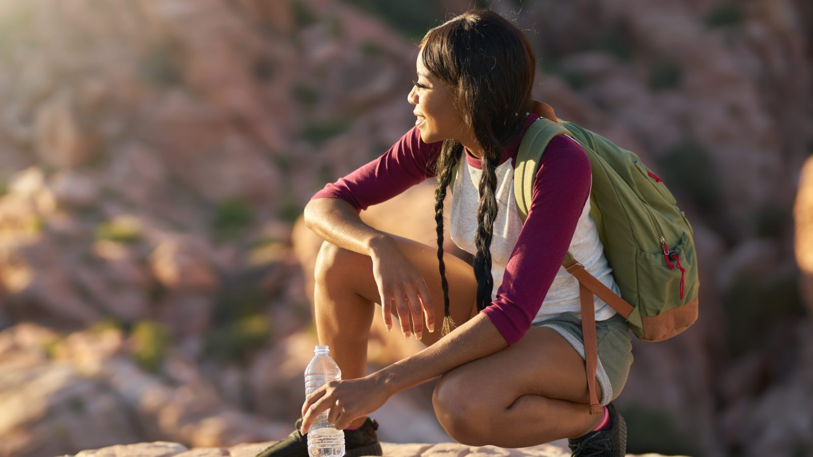woman wearing travel backpack relaxing on a rock with a waterbottle at sunset