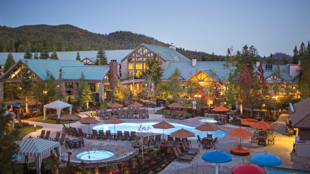 Exterior view of the Tenaya Lodge at Yosemite, with pools and trees in the foreground of the family friendly California resort