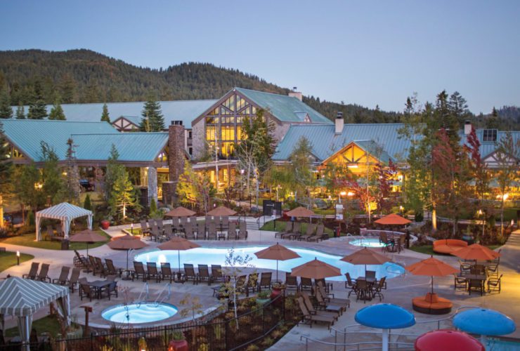 Exterior view of the Tenaya Lodge at Yosemite, with pools and trees in the foreground of the family friendly California resort