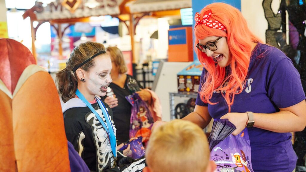 A costumed kid getting candy from a costumed adult at the Hershey's Chocolate World trick or treat event