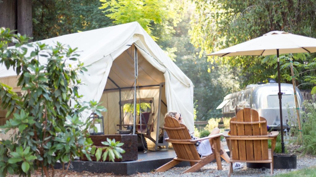 luxury tent in foreground with chairs and umbrella plus Airstream suite in background at AutoCamp Russian River