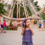 Girl eating ice cream in front of ferris wheel at amusement park
