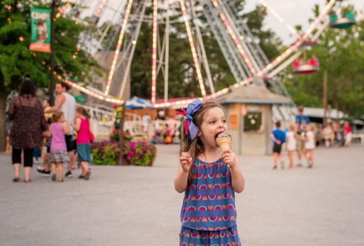 Girl eating ice cream in front of ferris wheel at amusement park