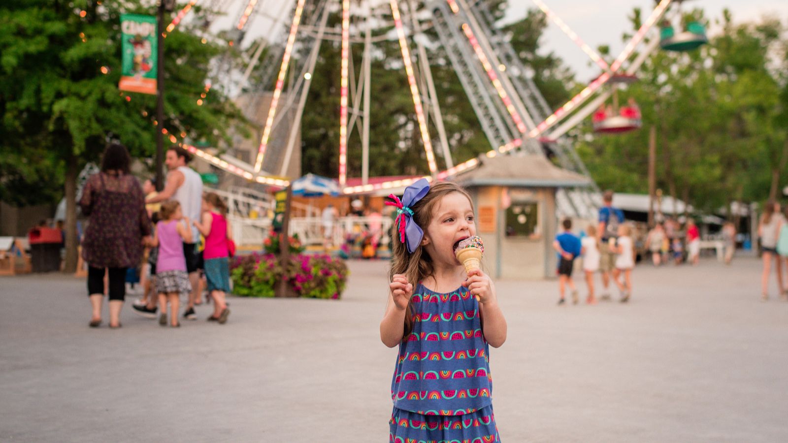 Girl eating ice cream in front of ferris wheel at amusement park