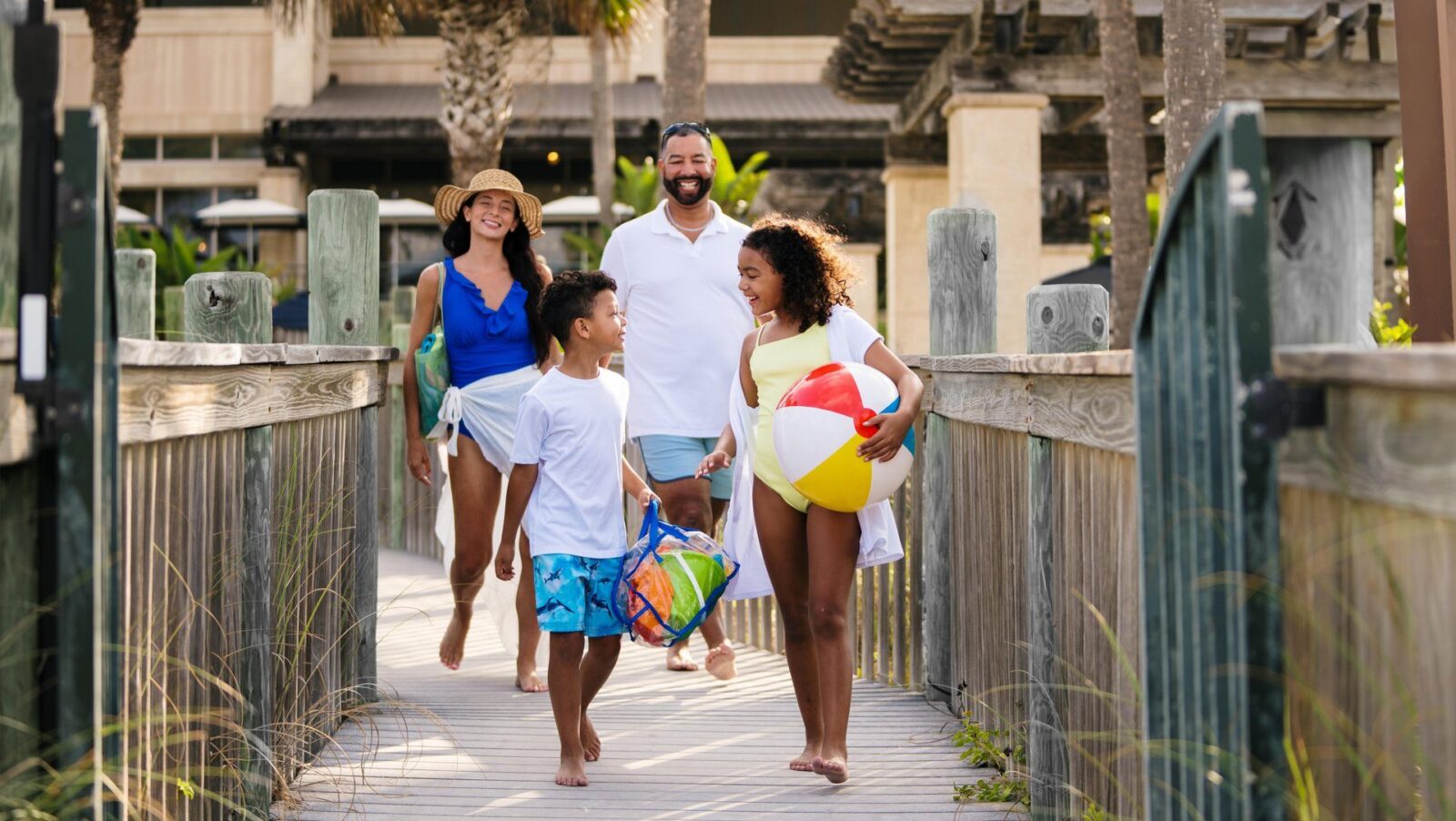 A family on a boardwalk heading to the beach with a beach ball