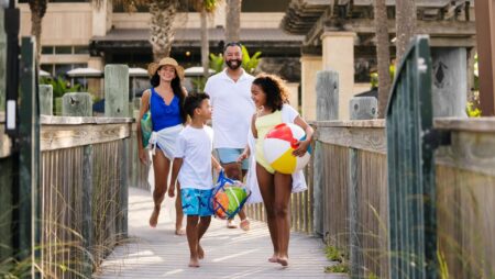 A family on a boardwalk heading to the beach with a beach ball