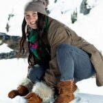 Person in the snow wearing Manitobah's Pacific Half Winter Boots and crouching down to touch the snow