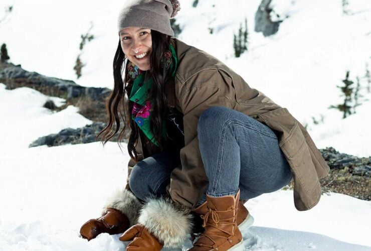 Person in the snow wearing Manitobah's Pacific Half Winter Boots and crouching down to touch the snow