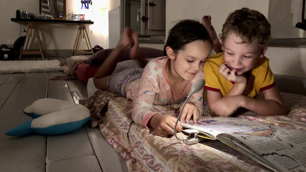 two children on vacation reading together at bedtime