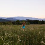 Two little girls running through a meadow with flowers with mountains in the distance
