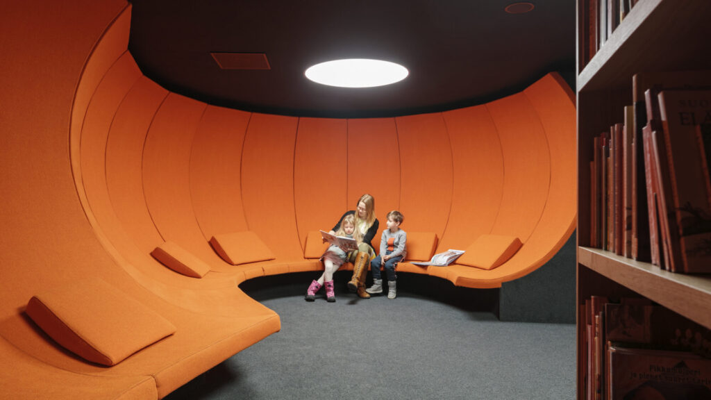 Adult and child sitting on bright orange tall seating at Oodi in Helsinki