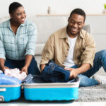 couple packing for the family with clothing in a teal suitcase