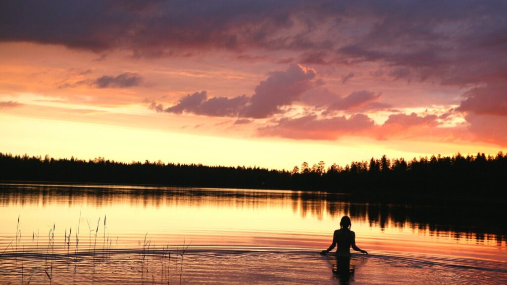 person wading into water with the sky lit up by the midnight sun in Finland