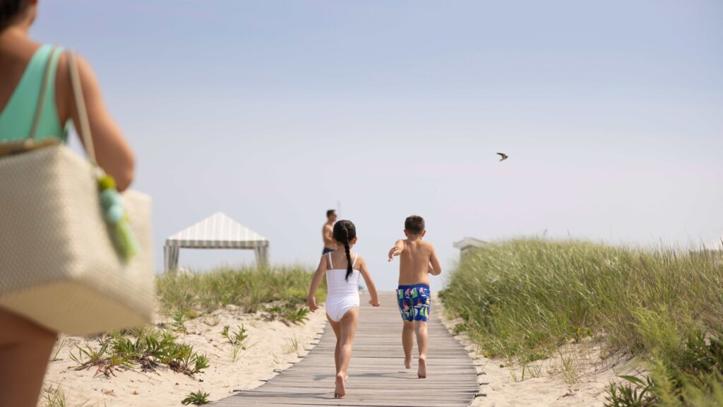A girl and a boy running down a boardwalk to the beach