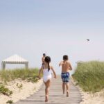 A girl and a boy running down a boardwalk to the beach