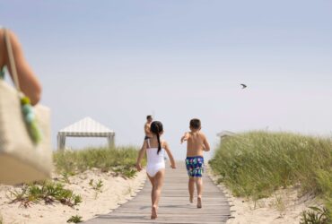 A girl and a boy running down a boardwalk to the beach