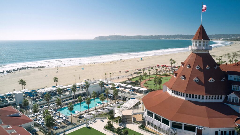 An aerial view of Hotel del Coronado with its red-roofed turret and the pool and beach in the distance