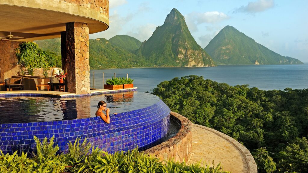 Seorang wanita sedang menyeruput minuman di kolam renang di Jade Mountain Resort dengan Piton di kejauhan