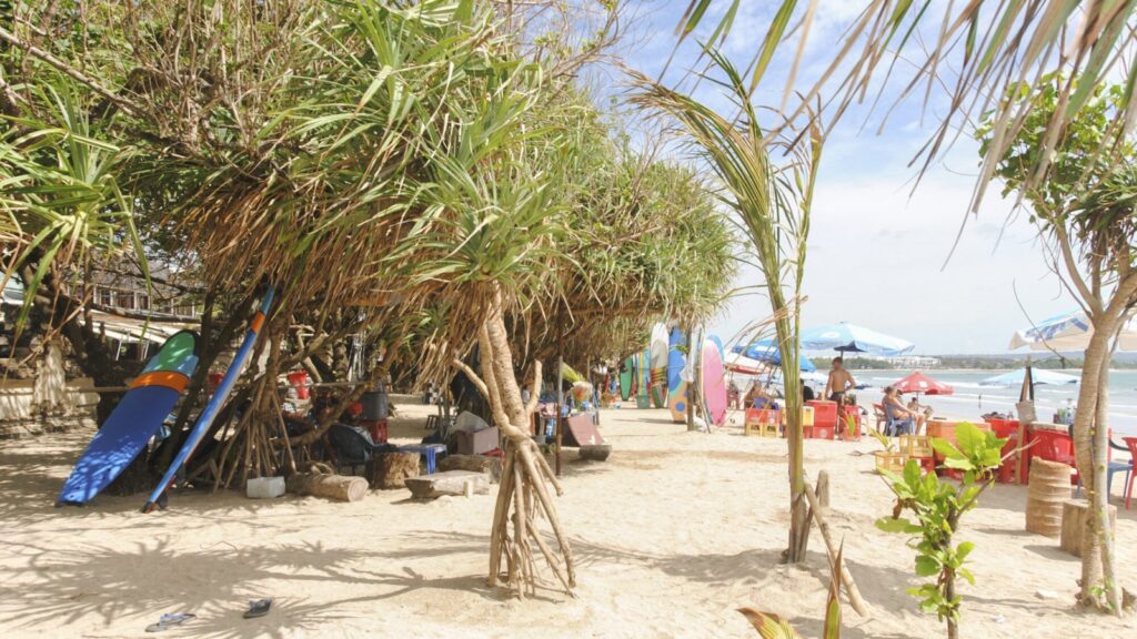 A beach in Kuta, Bali with surfboards leaning against trees