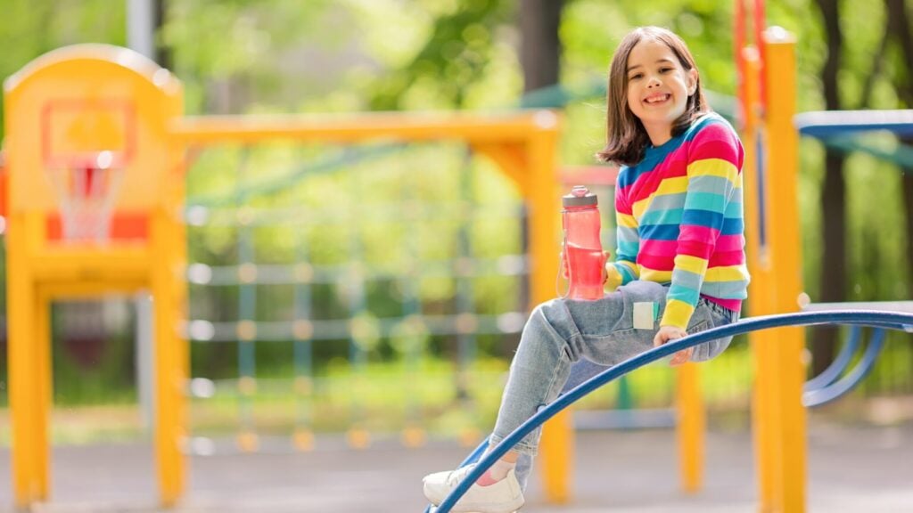 kid on a playground holding a water bottle