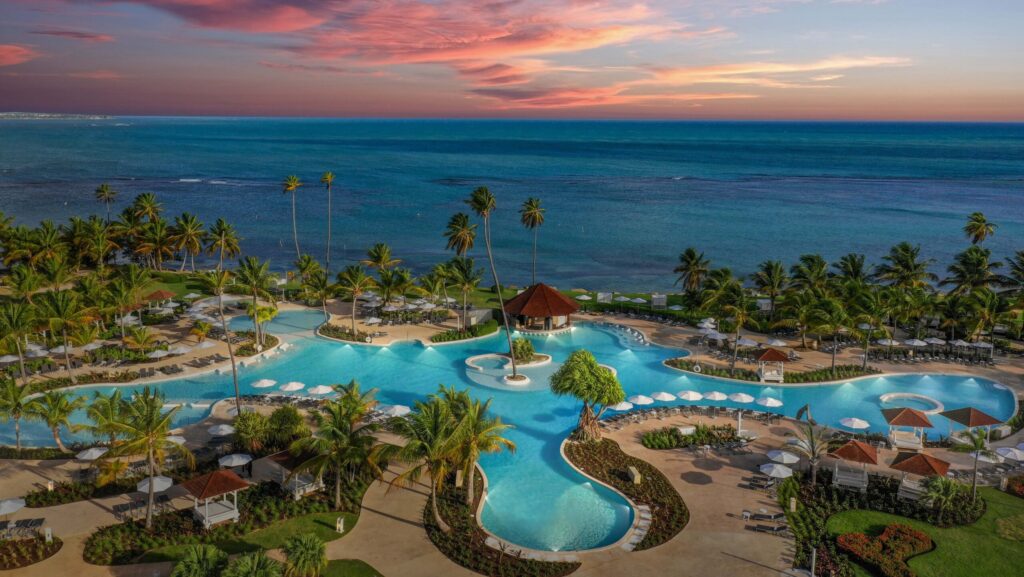 An aerial view of the lagoon-style pool at Hyatt Regency Grand Reserve Puerto Rico and the beach beyond it at sunset