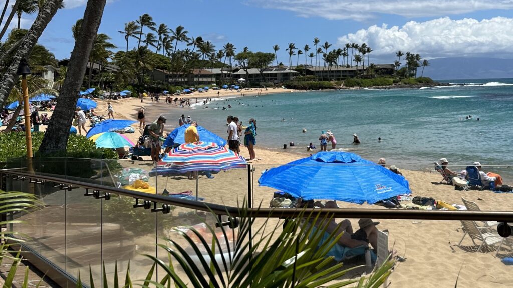People sitting in chairs and under umbrellas along Napili Bay in Maui