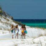 Four girls holding towels walking across white sand to get to the beach