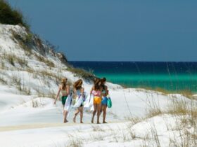 Four girls holding towels walking across white sand to get to the beach