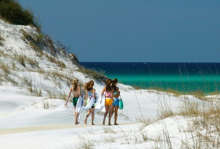 Four girls holding towels walking across white sand to get to the beach