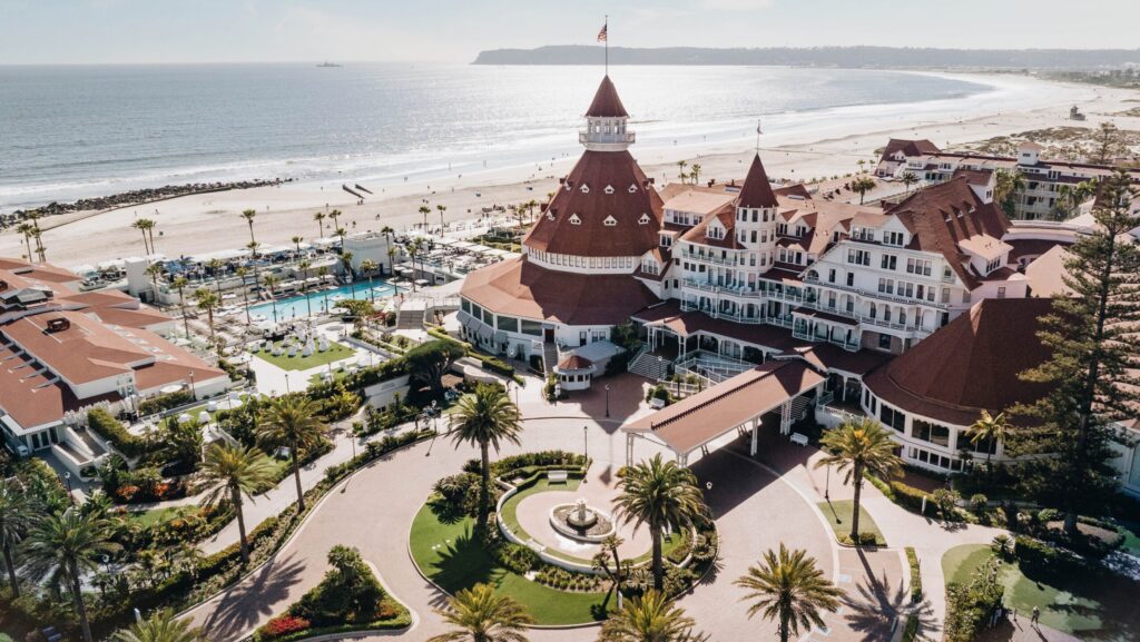 An aerial view of the Hotel del Coronado and its red turrets, pool, and beach area 